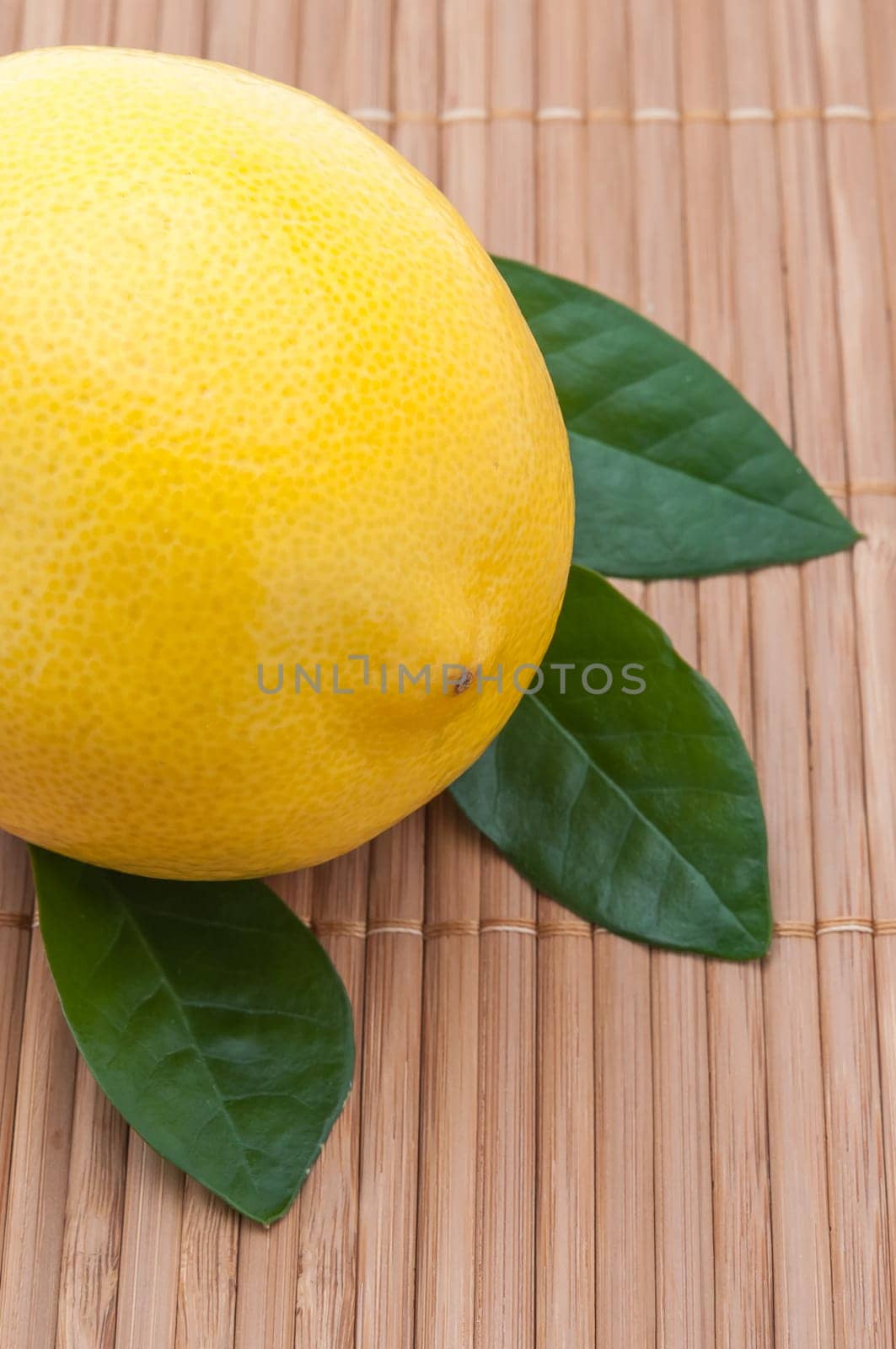 large yellow lemon with green leaves close-up on bamboo mat.