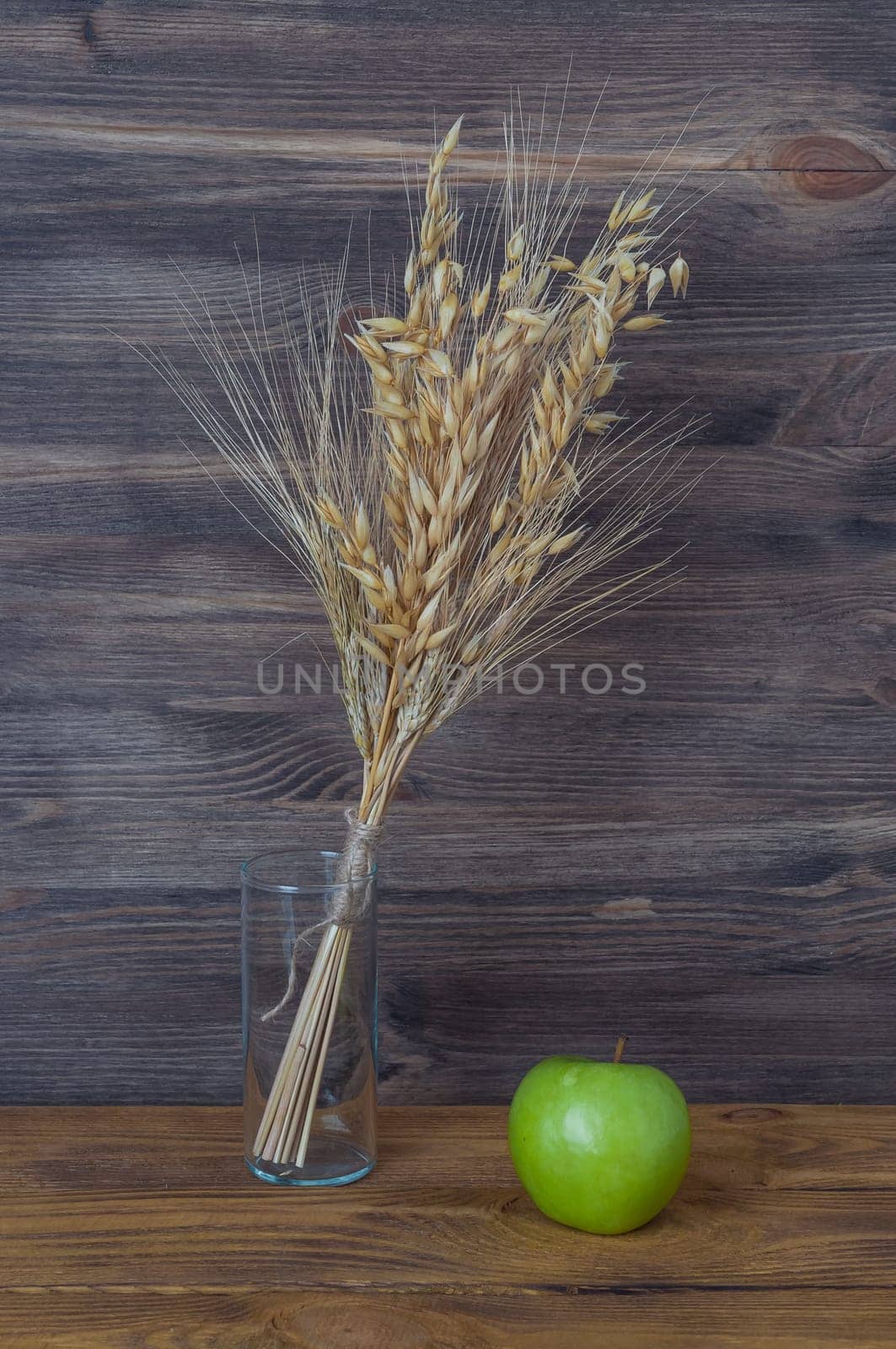 Spikes of wheat and barley in a glass vase on the background of wooden boards.