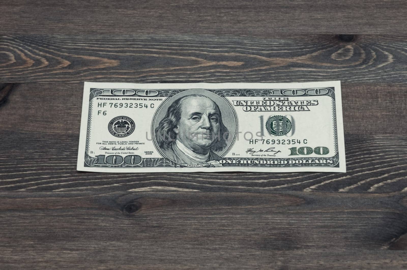 One hundred US dollars. One bill on a wooden table. Frontal side.