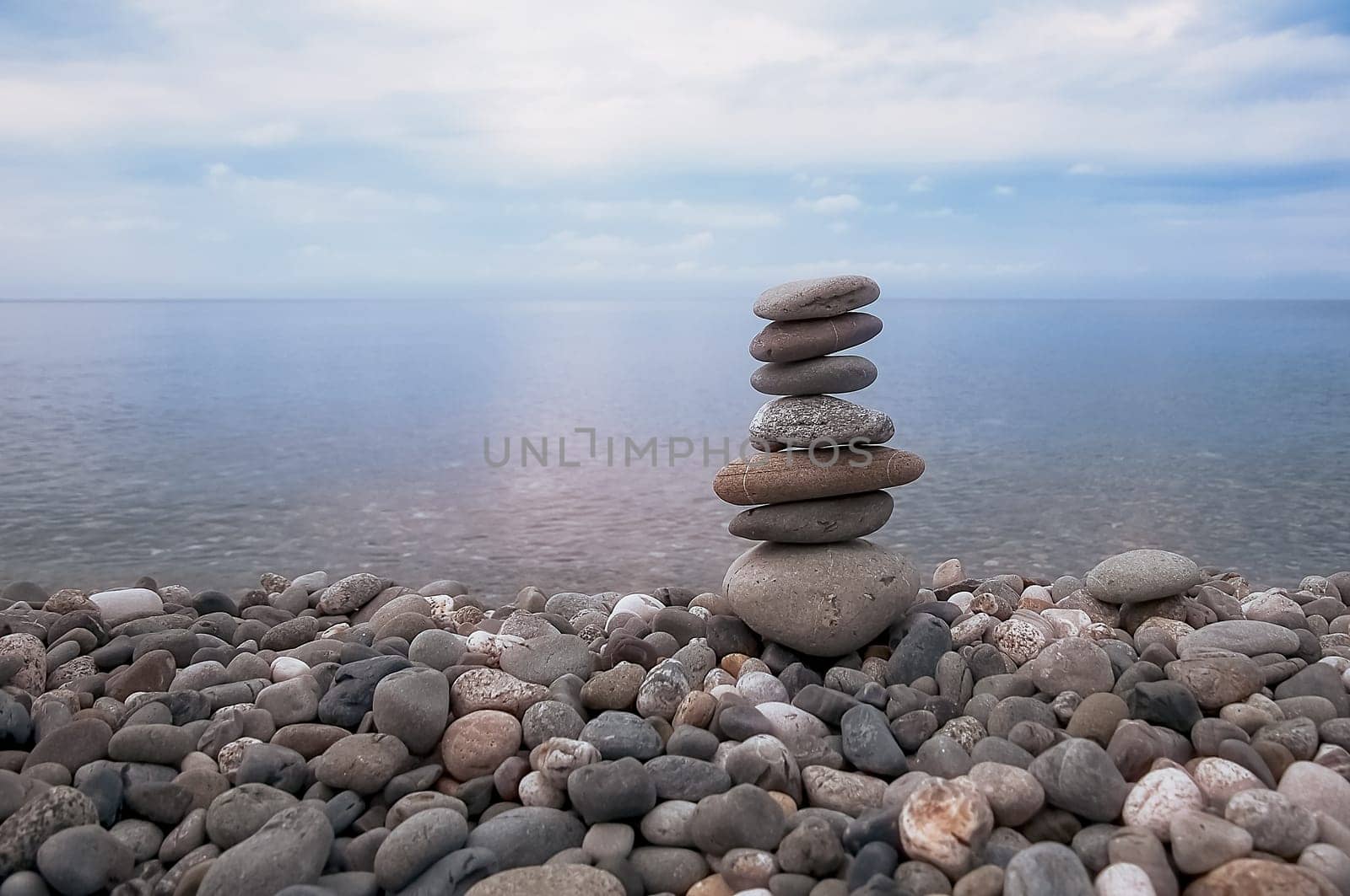 Sea, sky, rocky beach and pyramid of flat stones.