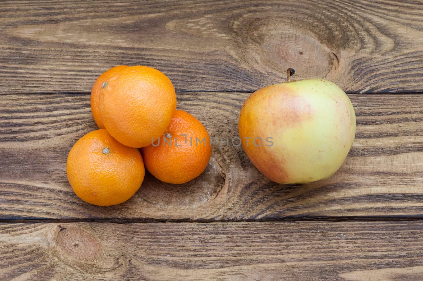 Four mandarins down a hill and an apple on a table of rough boards.