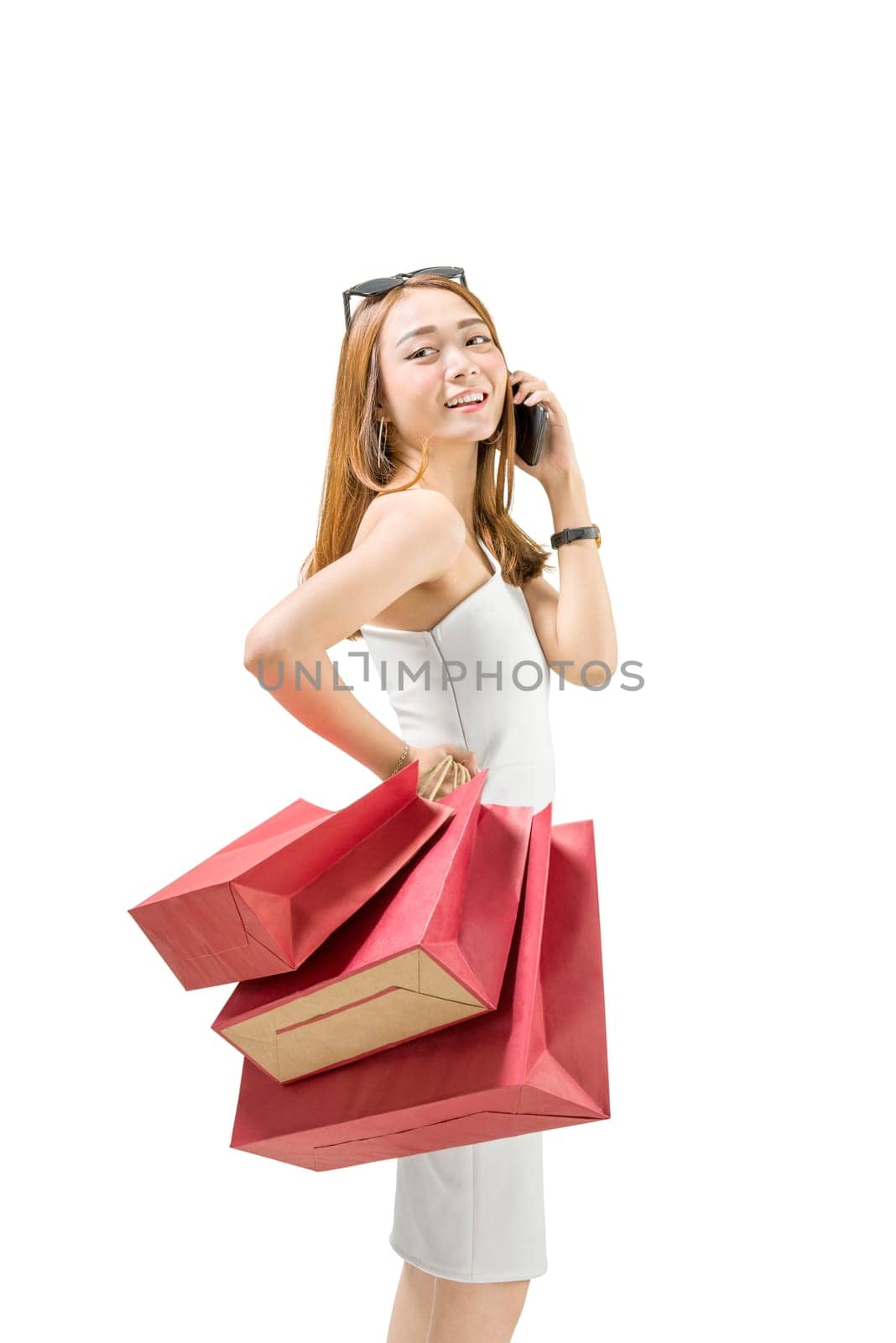 Smiling asian girl with shopping bags talking on mobile phone isolated over white background