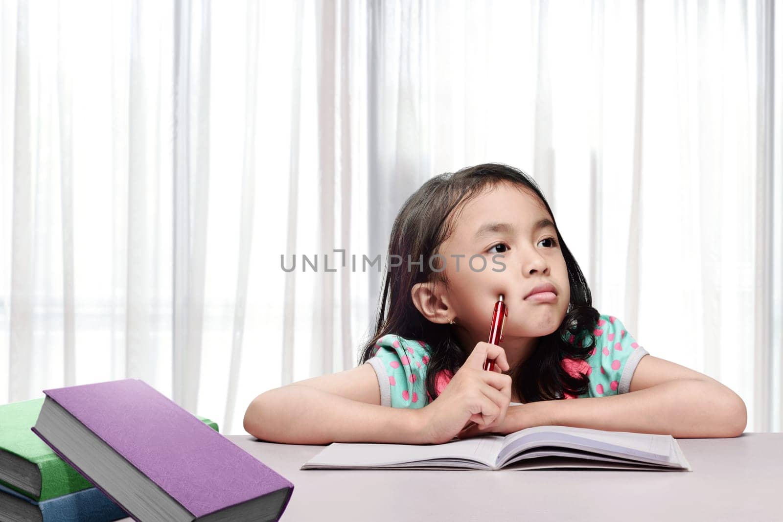 Little asian girl with book and pen thinking when doing homework at home