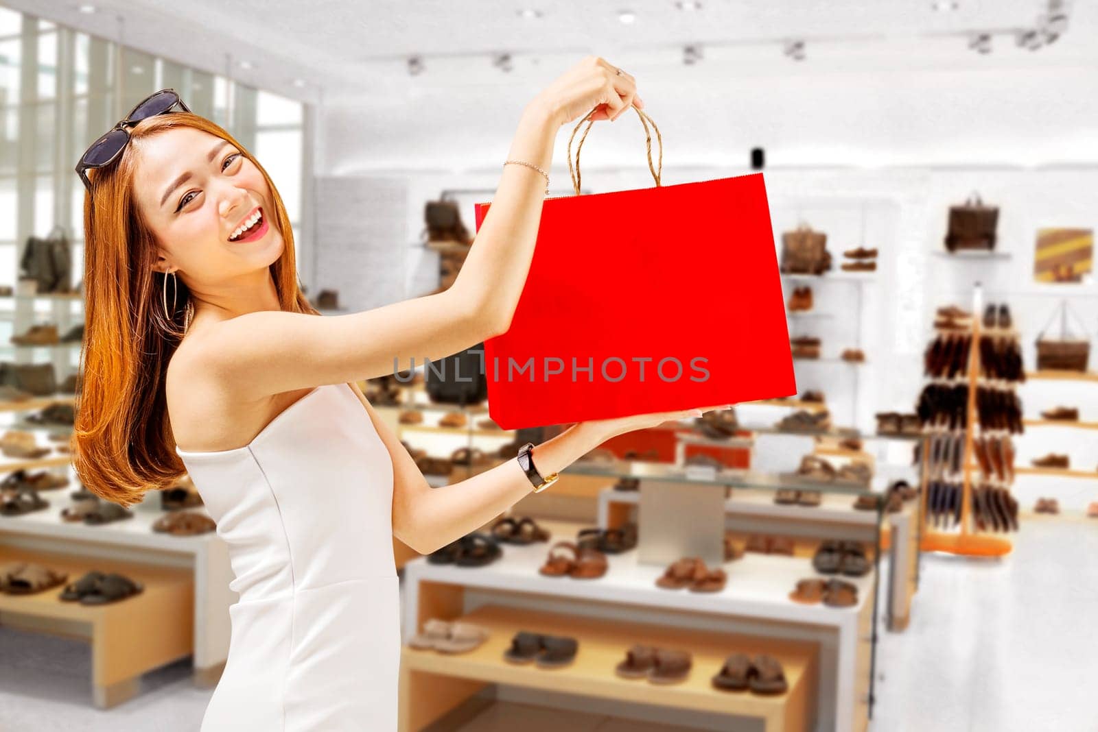 Young asian woman in white dress holding red shopping bags in front of store
