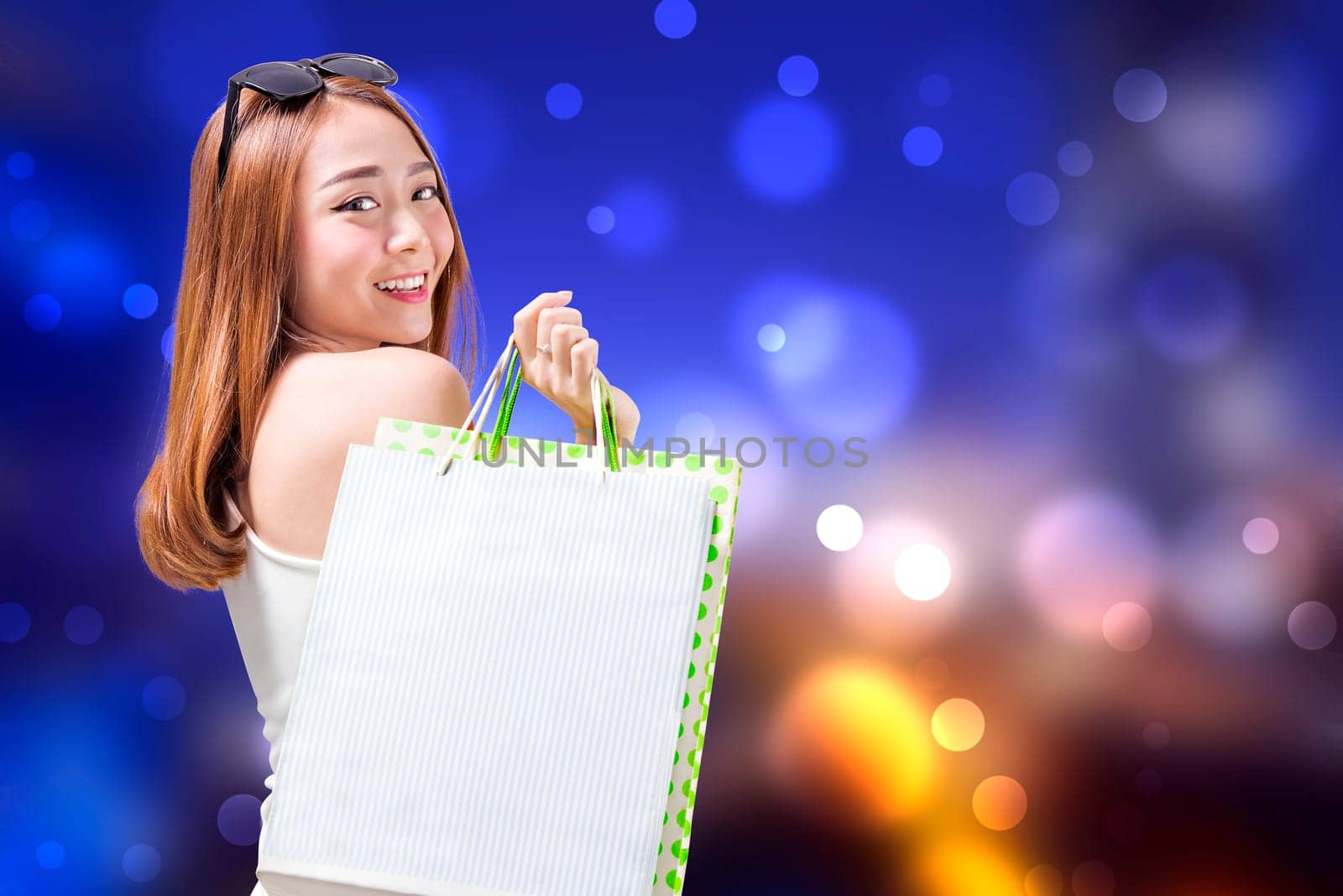 Young asian girl carrying some shopping bags with blurred lights background. Black friday concept
