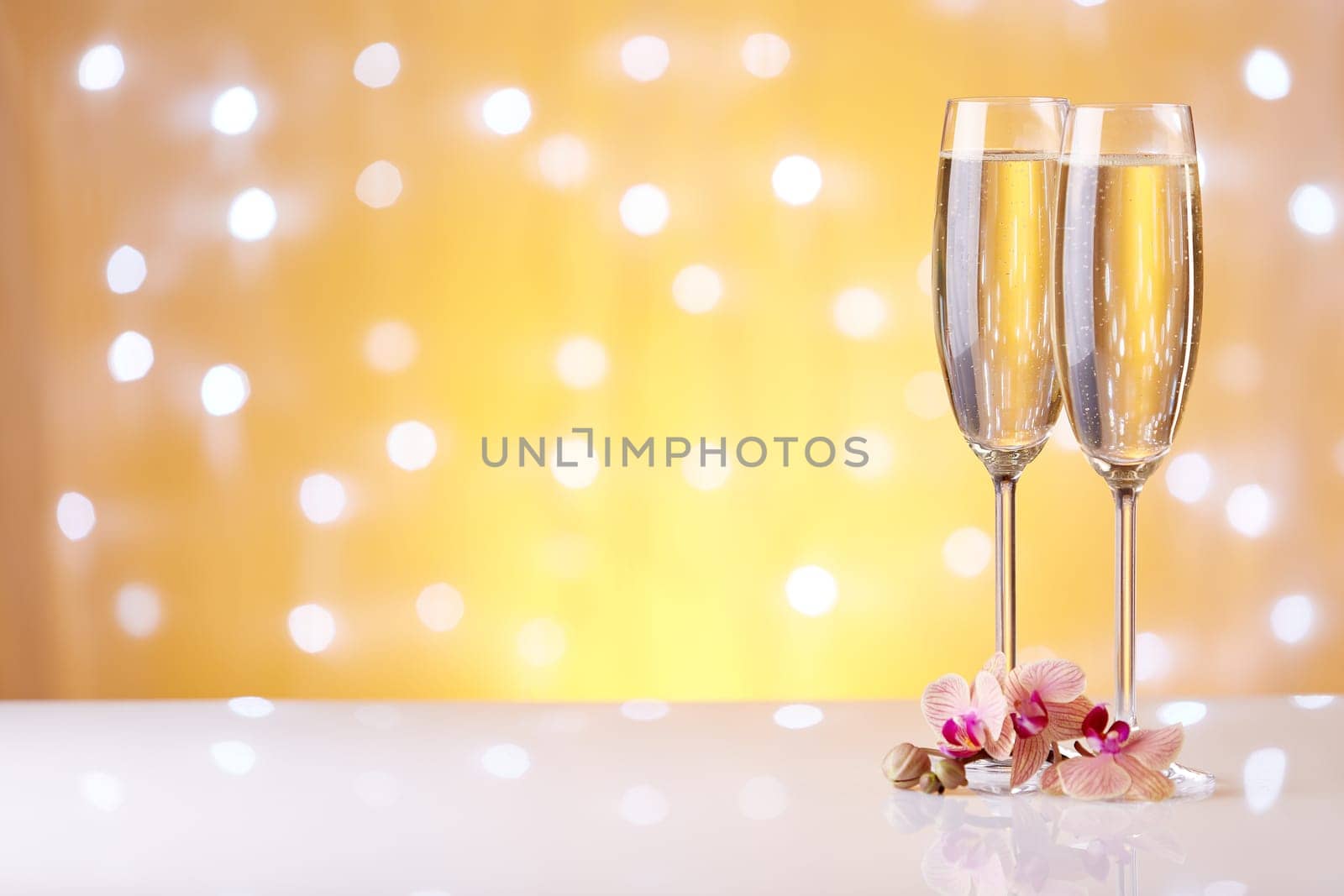 Two glasses with champange and flowers on a yellow background with lights of garland.