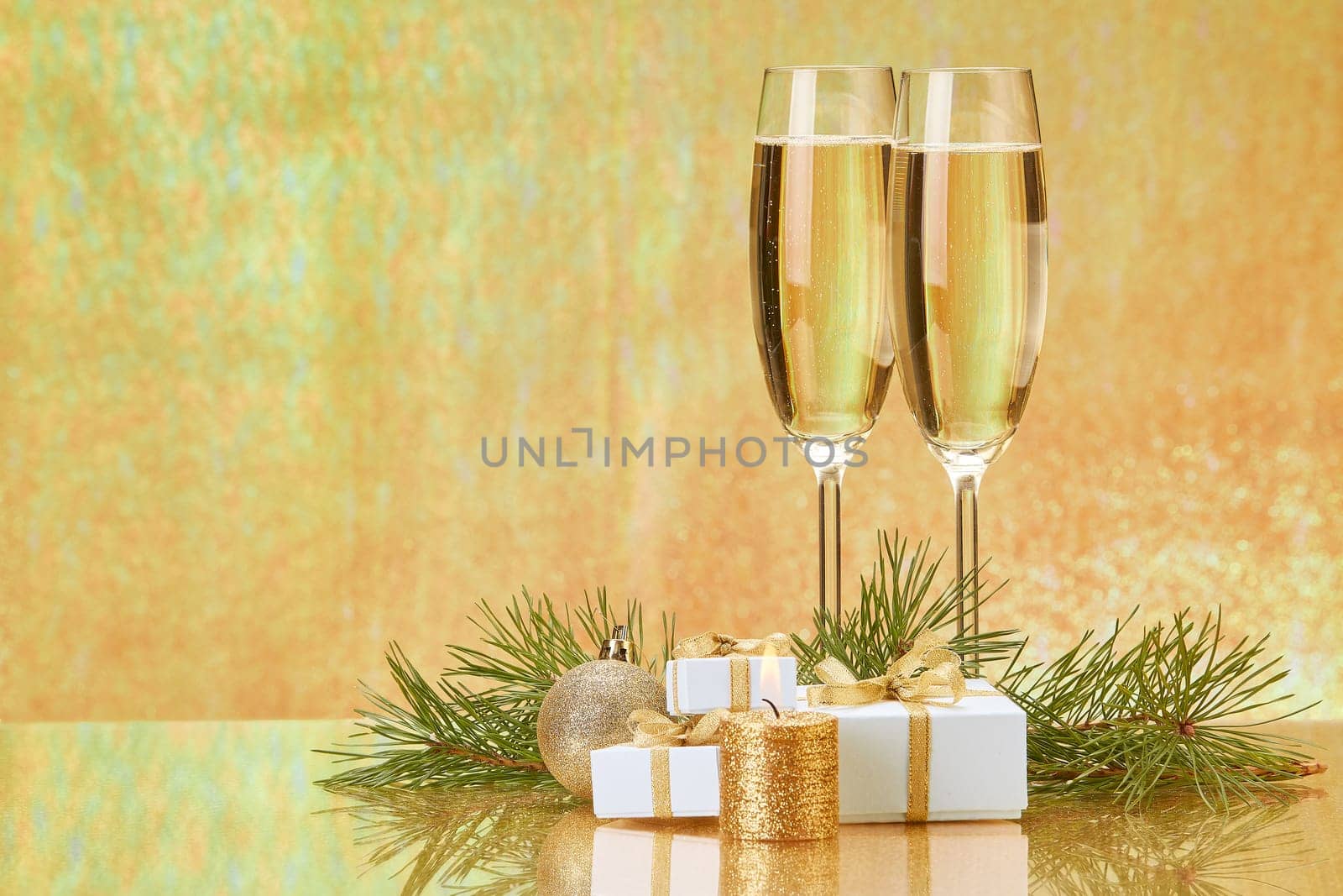 Two glasses with champange, fir tree branch, gift boxes and christmas decorations on a golden background. New year and Christmas.