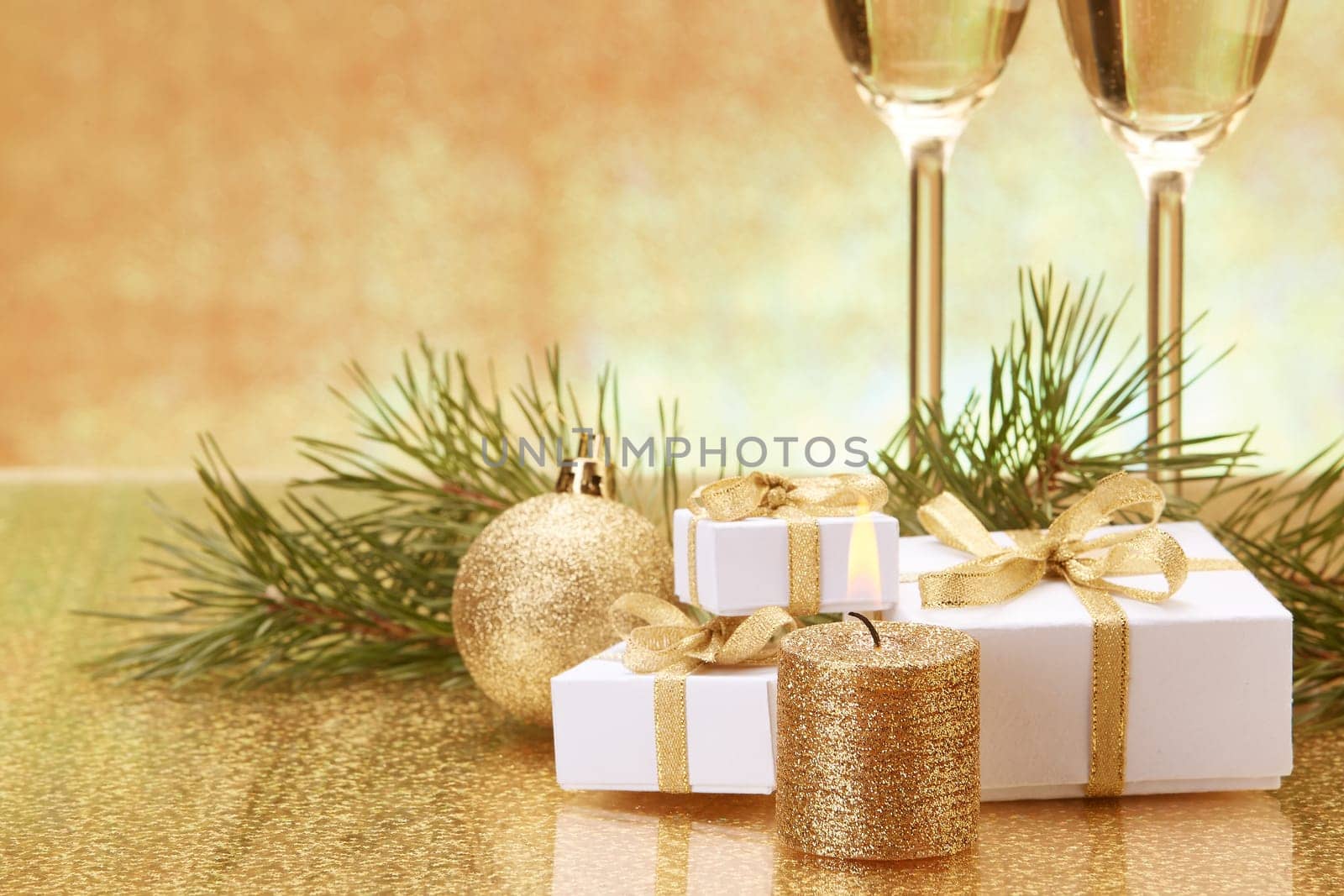 Two glasses with champange, fir tree branch, gift boxes and christmas decorations on a golden background. New year and Christmas.