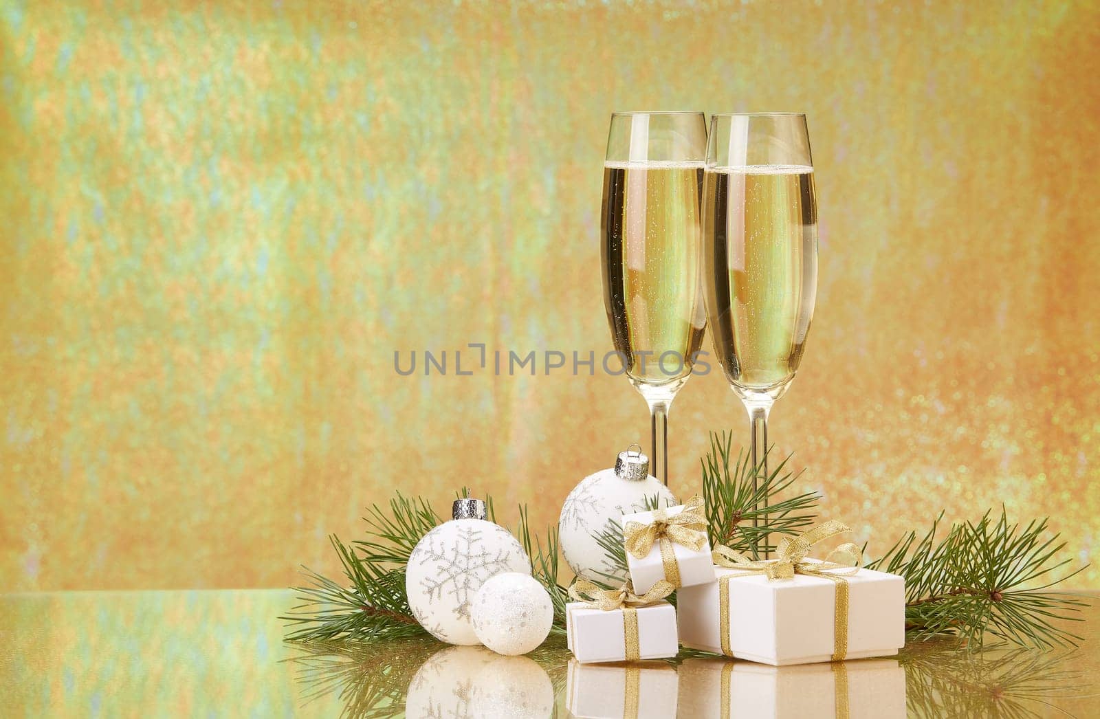 Two glasses with champange, fir tree branch, gift boxes and christmas decorations on a golden background. New year and Christmas.