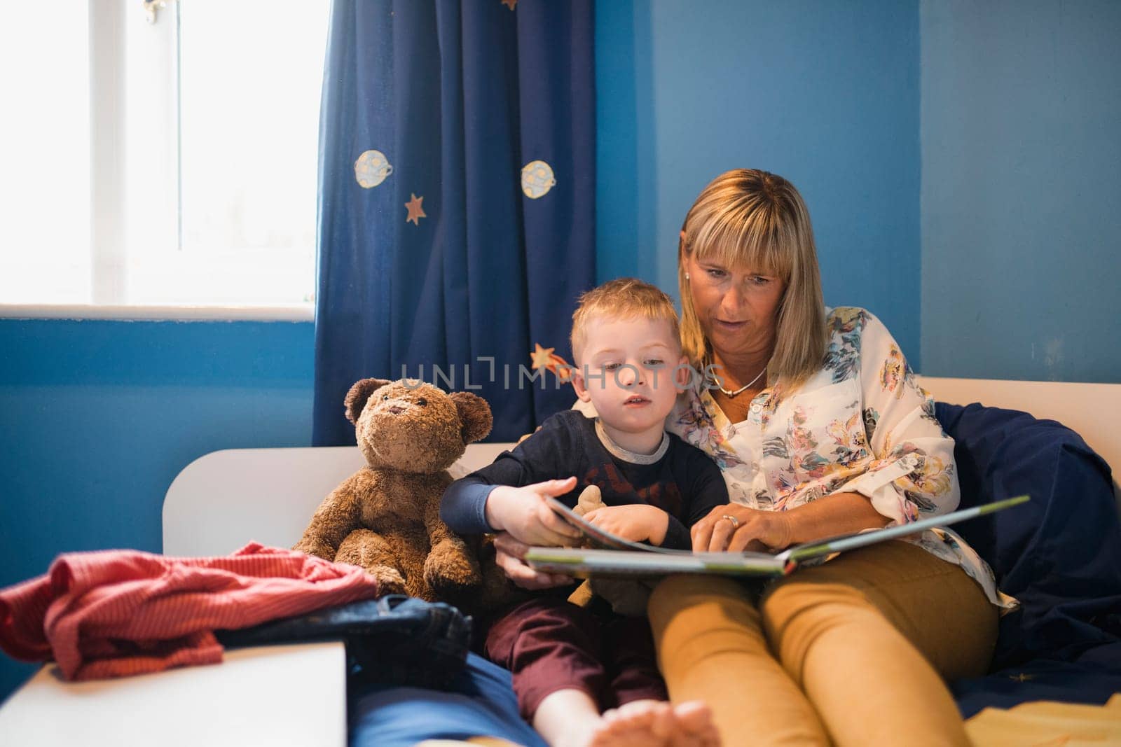 Grandmother and her grandson sitting in bed and reading a story before bedtime. Relaxing and spending some quality time together.
