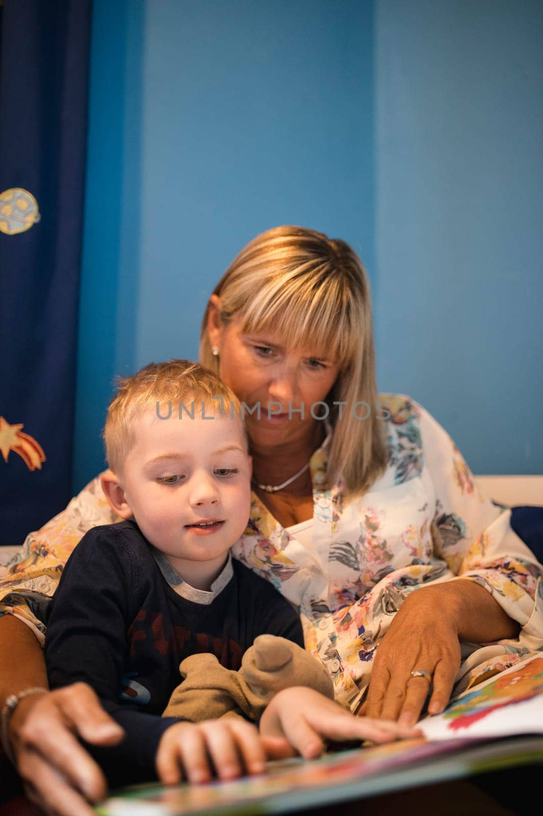 Grandmother and her grandson sitting in bed and reading a story before bedtime. Relaxing and spending some quality time together.