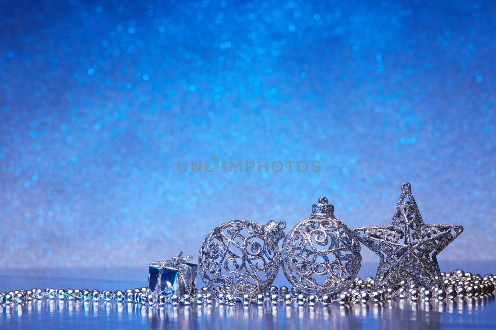Christmas decoration with silver balls, star, gift box and garlands lying on a blue background. New year and Christmas background with copy space for text. Greeting card.
