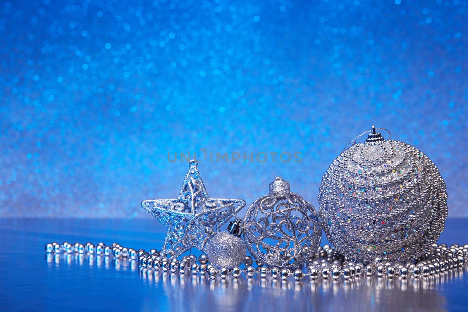 Christmas decoration with silver balls, star, gift box and garlands lying on a blue background. New year and Christmas background with copy space for text. Greeting card.