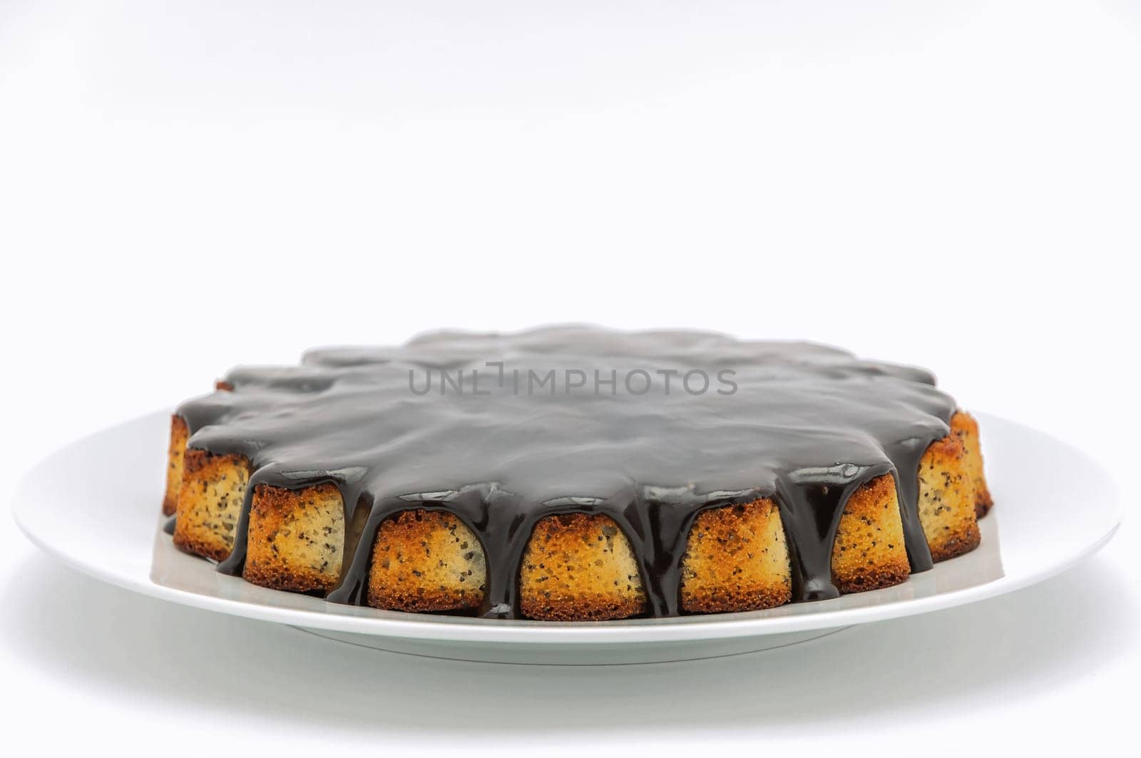 Round cake with poppy seeds covered in chocolate on a plate on a white background.