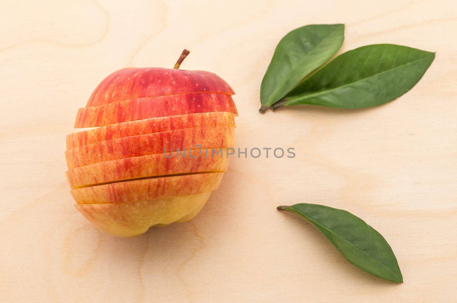 The sliced apple that retained its shape rests on a wooden table with green flatteries.