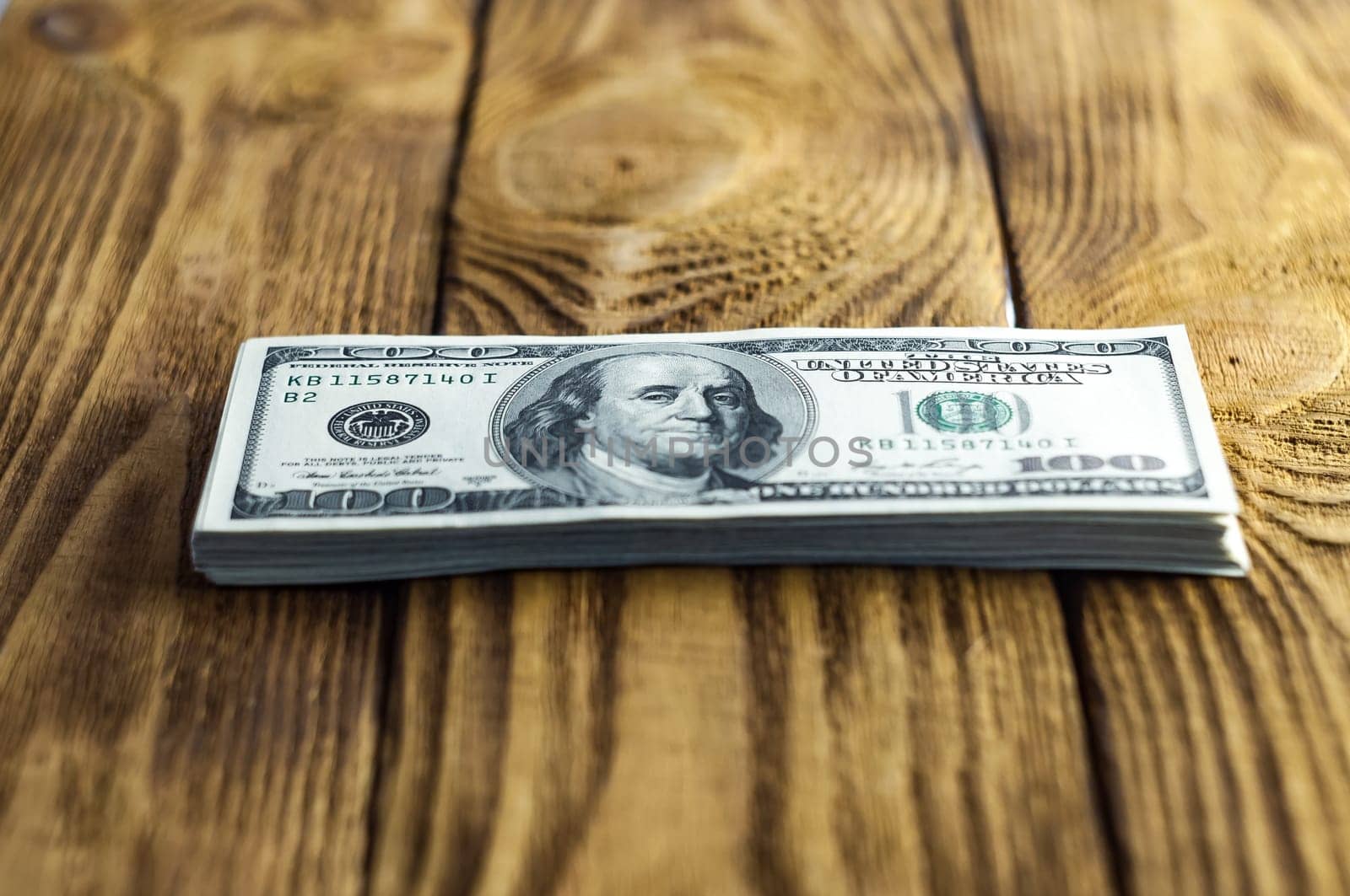 A pack of one hundred dollar bills on a wooden table. Small depth of field. Focus on the President Franklin.