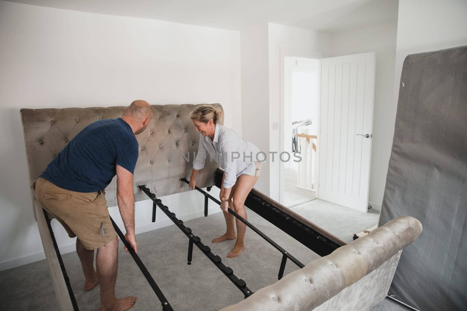 Mature couple are moving in to their new home. They are positioning their bed frame in the bedroom.