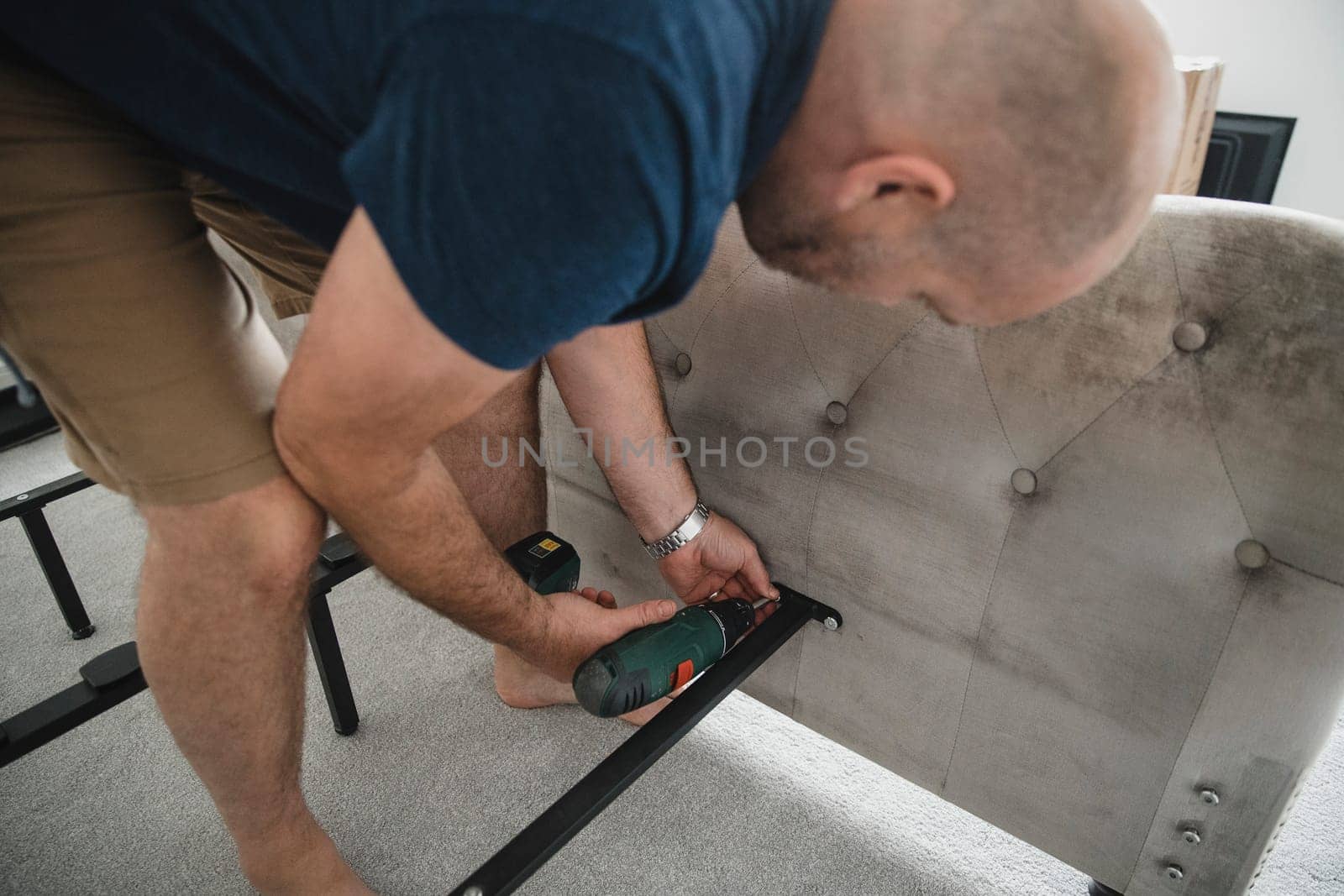 Mature man is using a power drill to put together a bed in his new home.