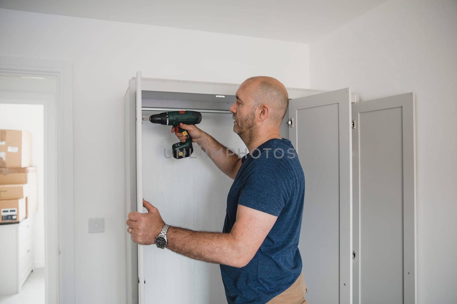 Mature man is building a wardrobe in the bedroom of his new home.