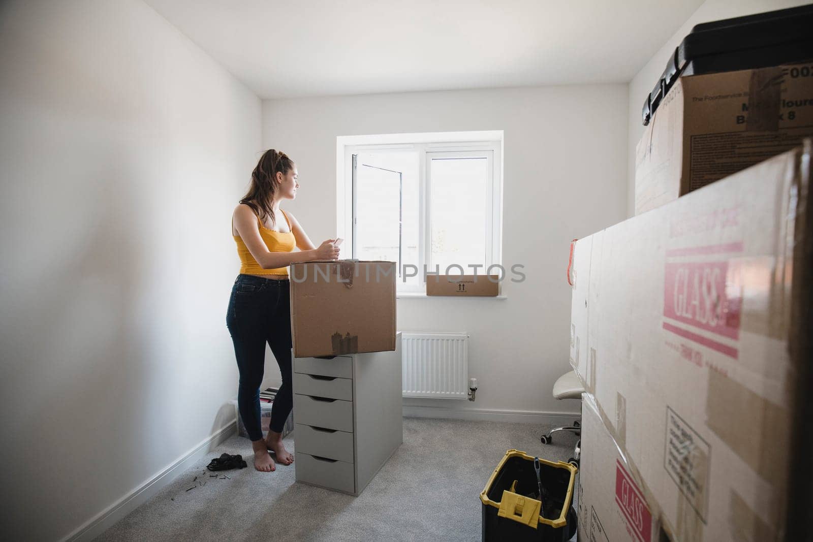 Teenage girl is taking a break from unpacking and is using her smart phone in her new bedroom.