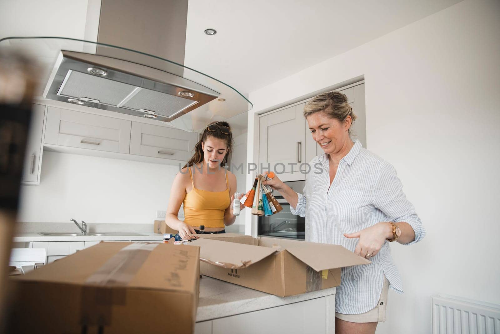 Mature woman and her teenage daughter have moved in to a new home and are unpacking boxes in the kitchen together.