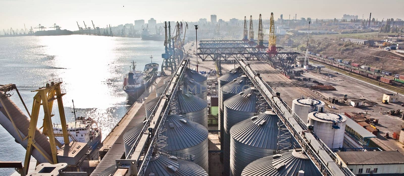 Grain from silos being loaded onto cargo ship on conveyor belt with freight train