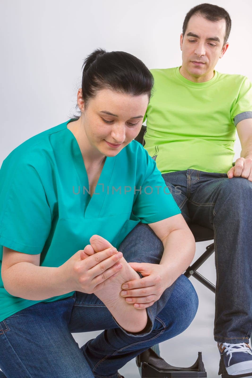 Female physiotherapist massaging foot of young man in wheelchair. People, healthy and care concept.