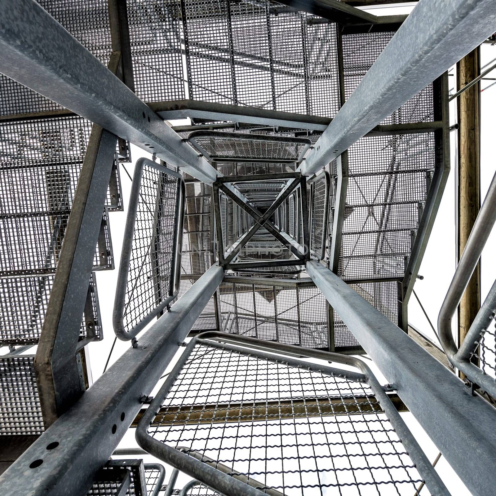 Square metal tower construction with staircase against white background