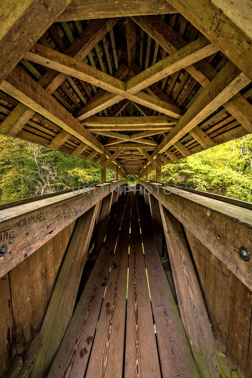 Long wooden beamed pedestrian bridge with roof and graffiti