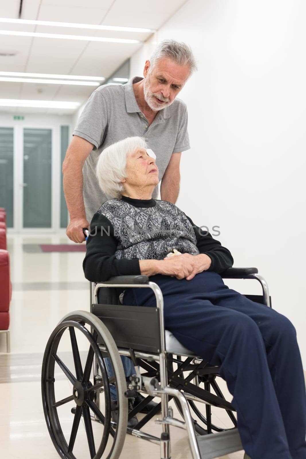 Middle aged man helping and making company to elderly 95 years old woman sitting in the wheelchair. Social aid for retirement citizens concept.