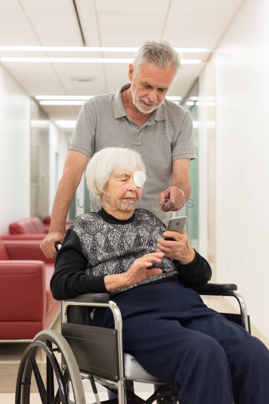 Middle aged man showing and helping elderly 95 years old woman sitting at the wheelchair how to use modern mobile phone application to monitor her therapy and entertain herself.