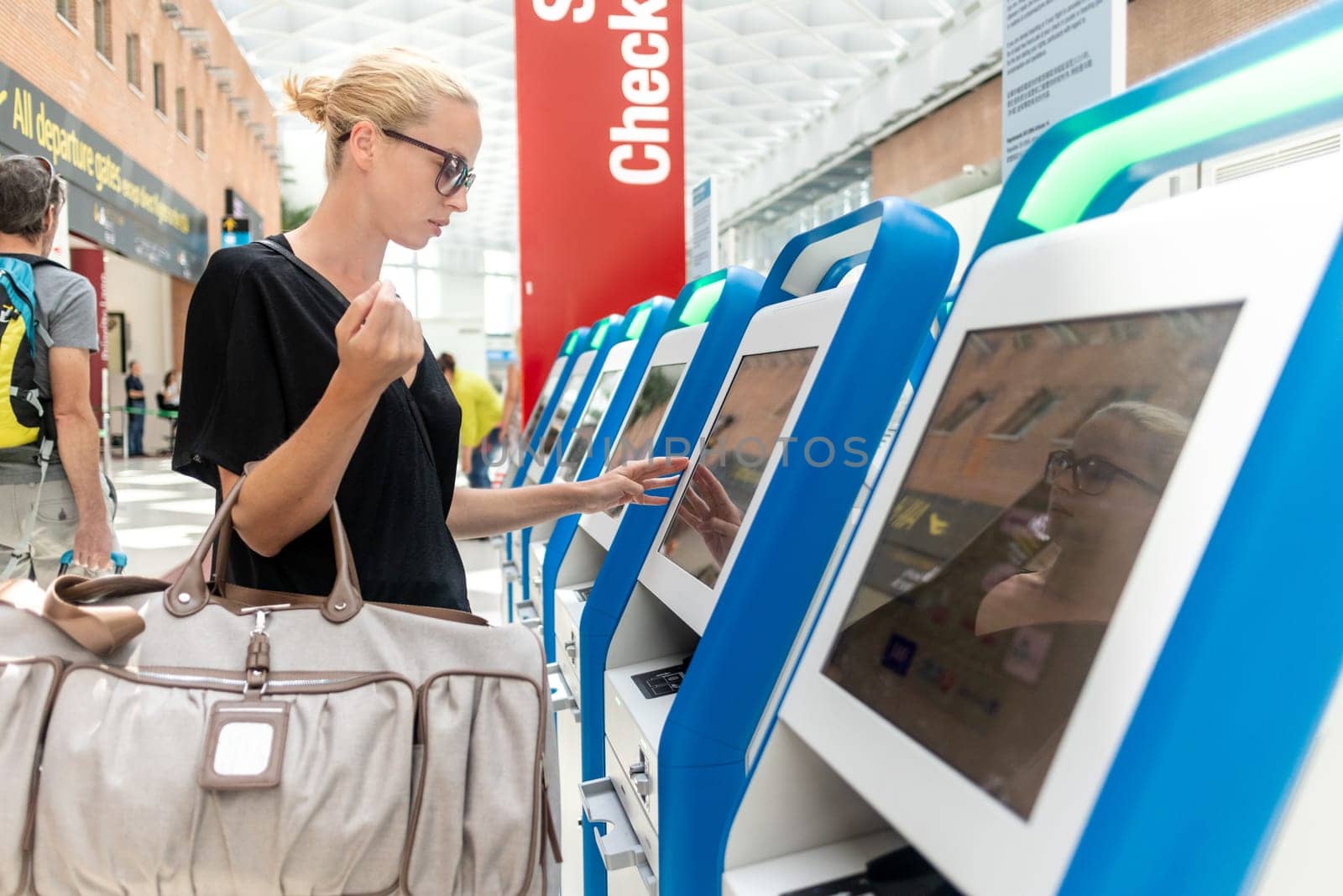 Casual caucasian woman using smart phone application and check-in machine at the airport getting the boarding pass. Modern technology on airport.