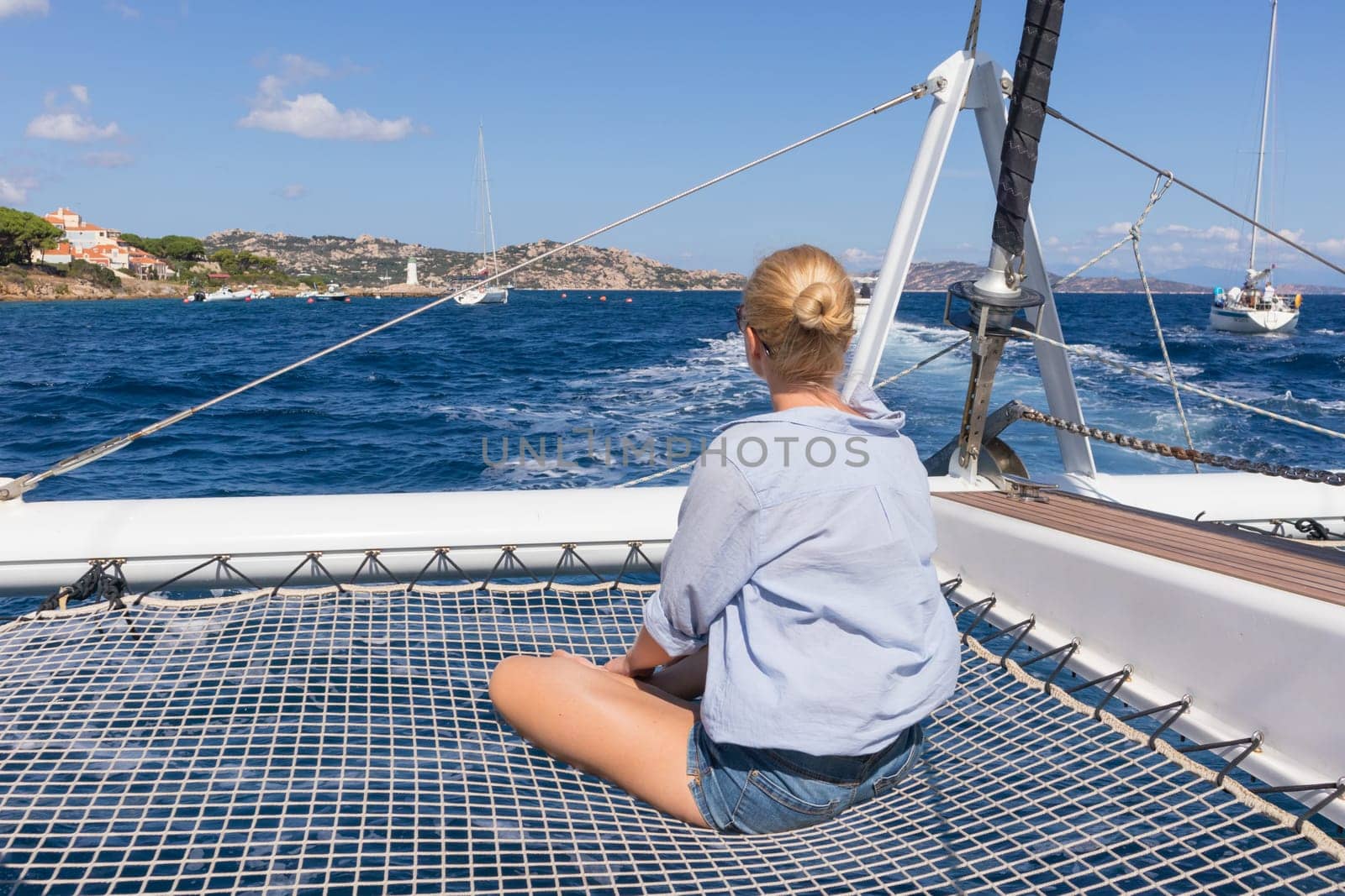 Casual woman relaxing on a summer vacations sailin cruise, sitting on a luxury catamaran, sailing in Maddalena Archipelago, Sardinia, Italy.