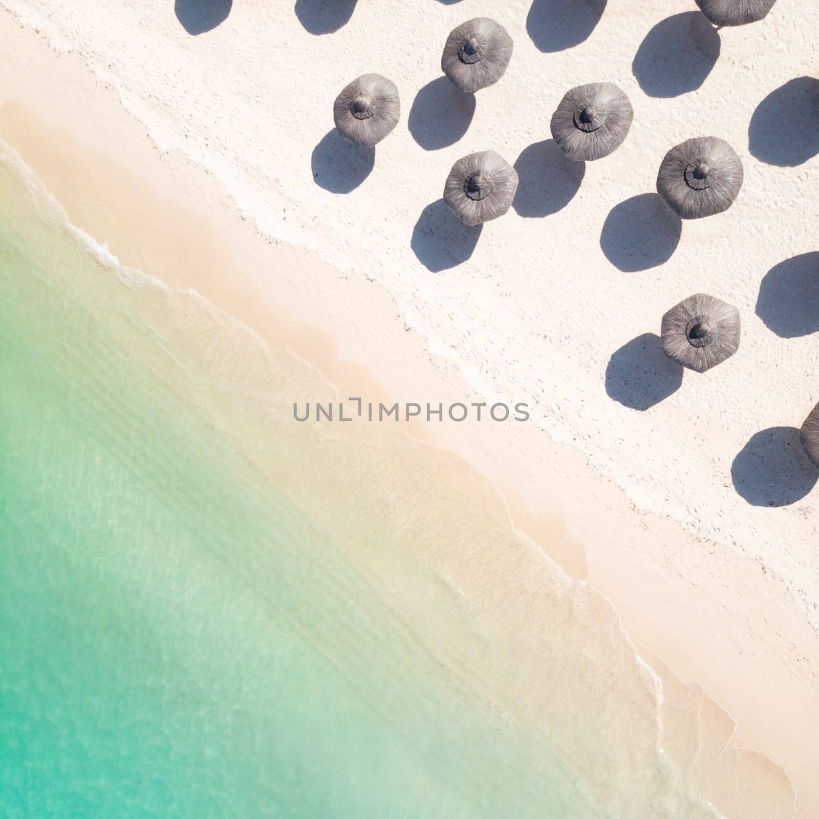 Aerial view of amazing tropical white sandy beach with palm leaves umbrellas and turquoise sea, Mauritius.