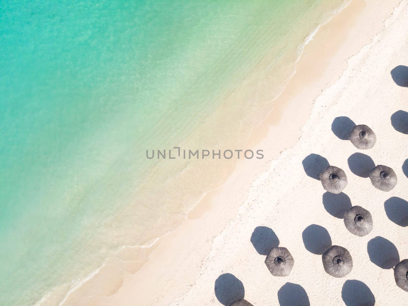Aerial view of amazing tropical white sandy beach with palm leaves umbrellas and turquoise sea, Mauritius.