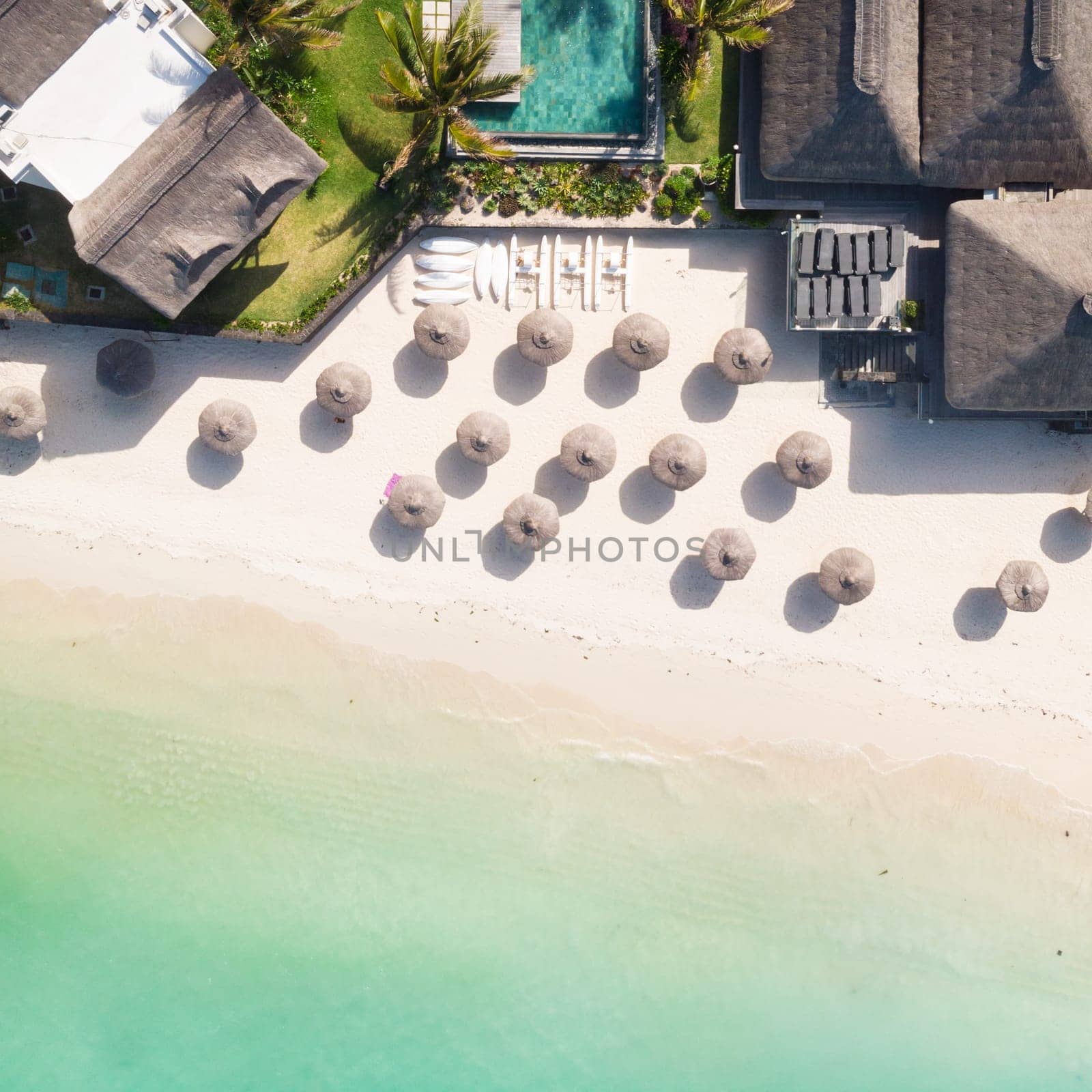 Aerial view of beautiful tropical beach front hotel resort with swimming pool, palm leaves umbrellas and turquoise sea. Paradise destination for vacations in Mauritius.