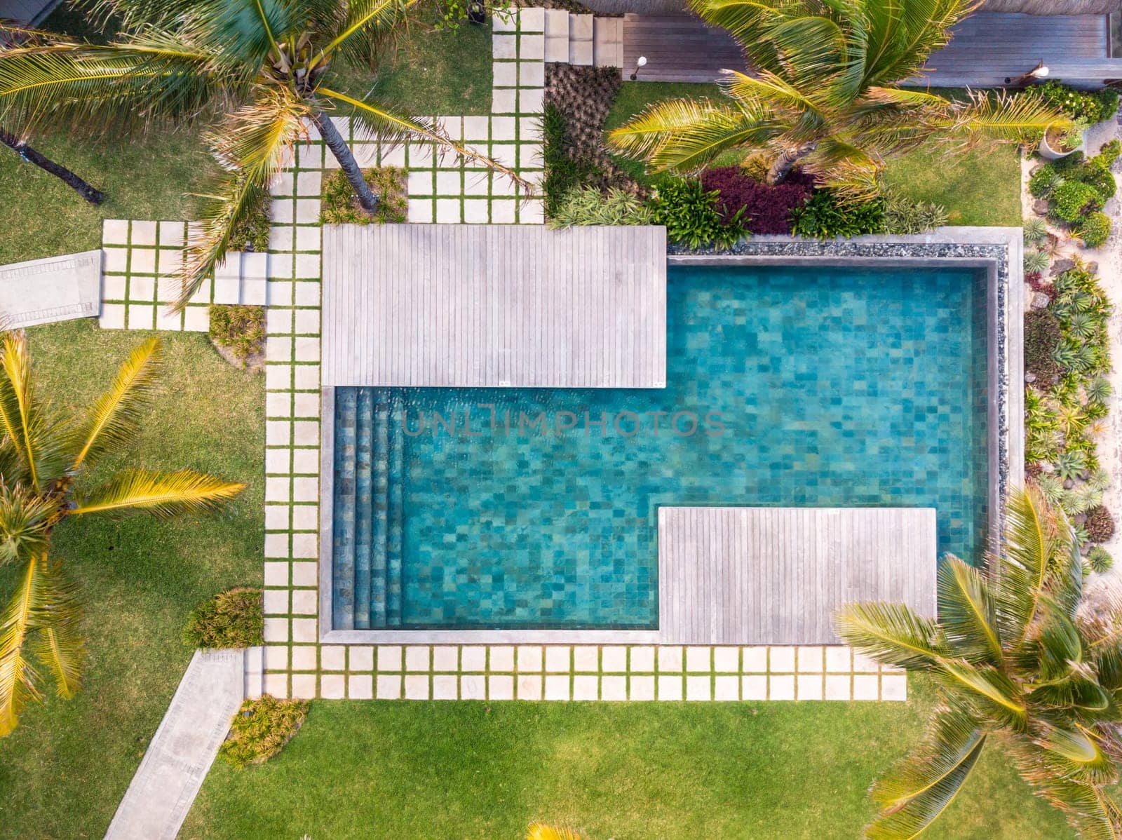 Aerial view of luxury hotel resort with swimming pool with stair and wooden deck surrounded by palm trees. Paradise destination for vacations.