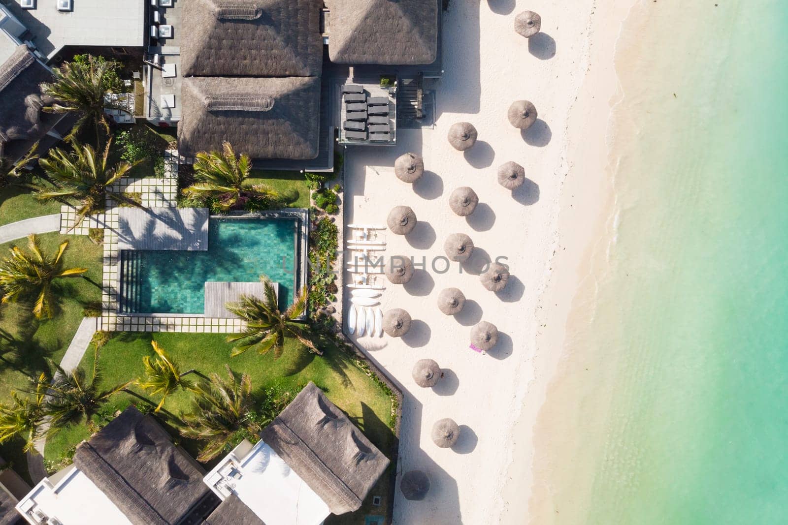 Aerial view of beautiful tropical beach front hotel resort with swimming pool, palm leaves umbrellas and turquoise sea. Paradise destination for vacations in Mauritius.