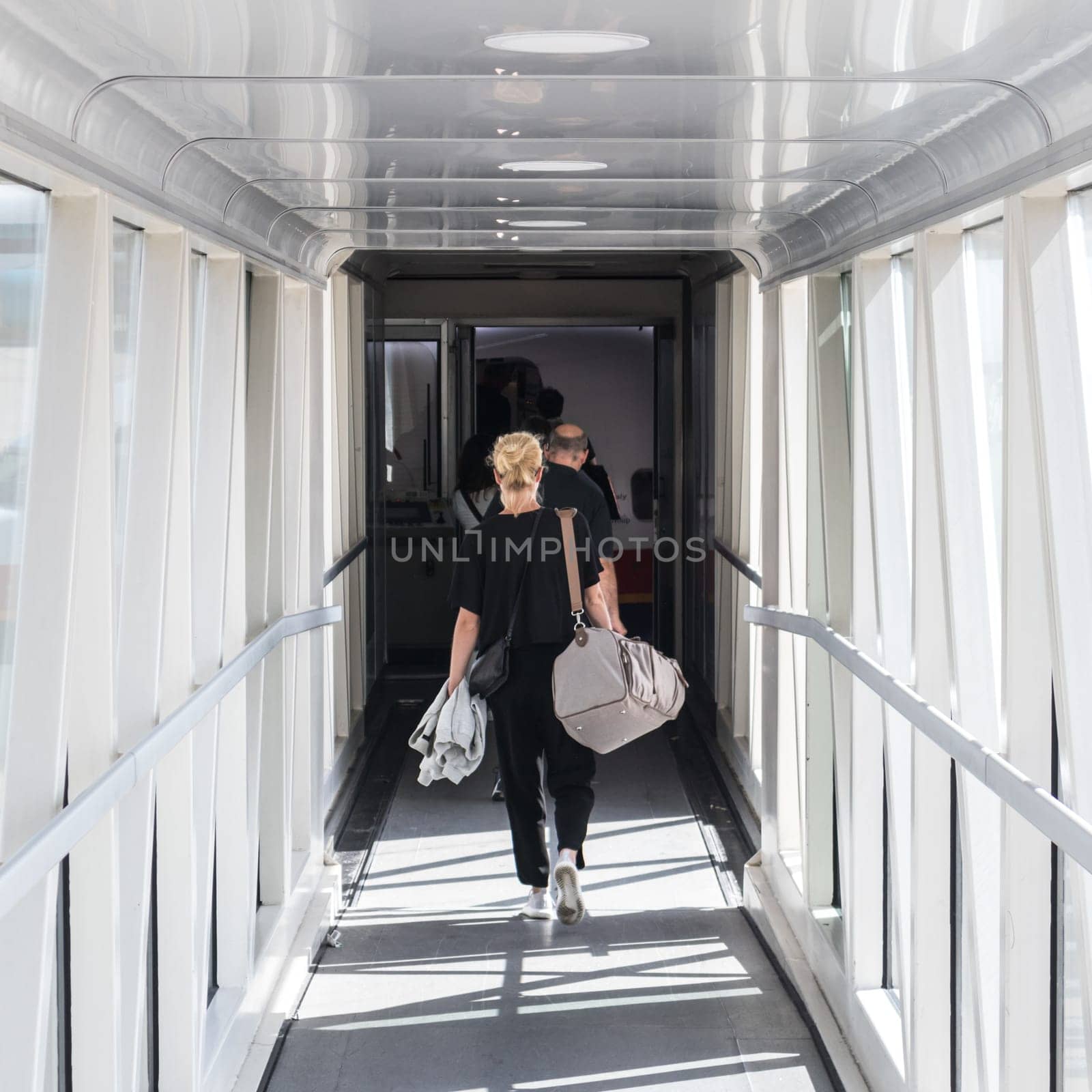 Airplane Boarding. Casual female passenger carrying the hand luggage bag, walking the airplane boarding corridor.