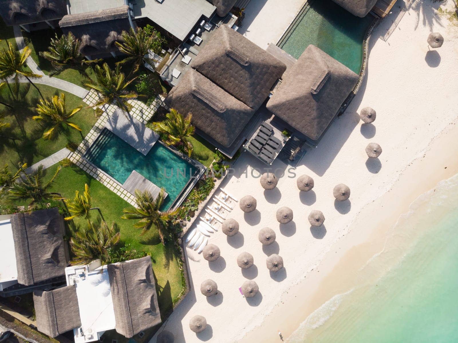 Aerial view of beautiful tropical beach front hotel resort with swimming pool, palm leaves umbrellas and turquoise sea. Paradise destination for vacations in Mauritius.
