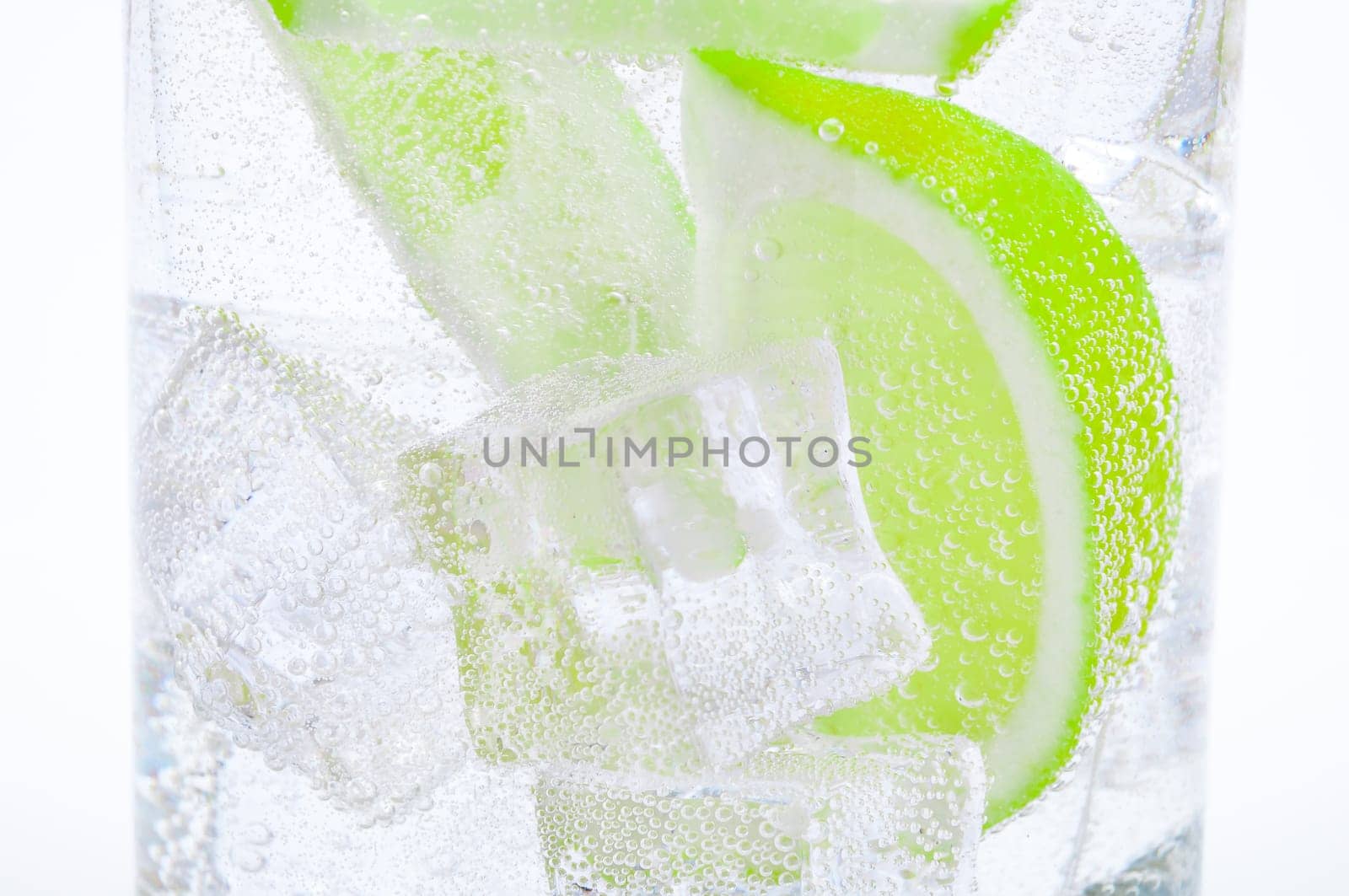 Drink from ice, lumps of f juicy green lime and crystal clear water in a glass.
