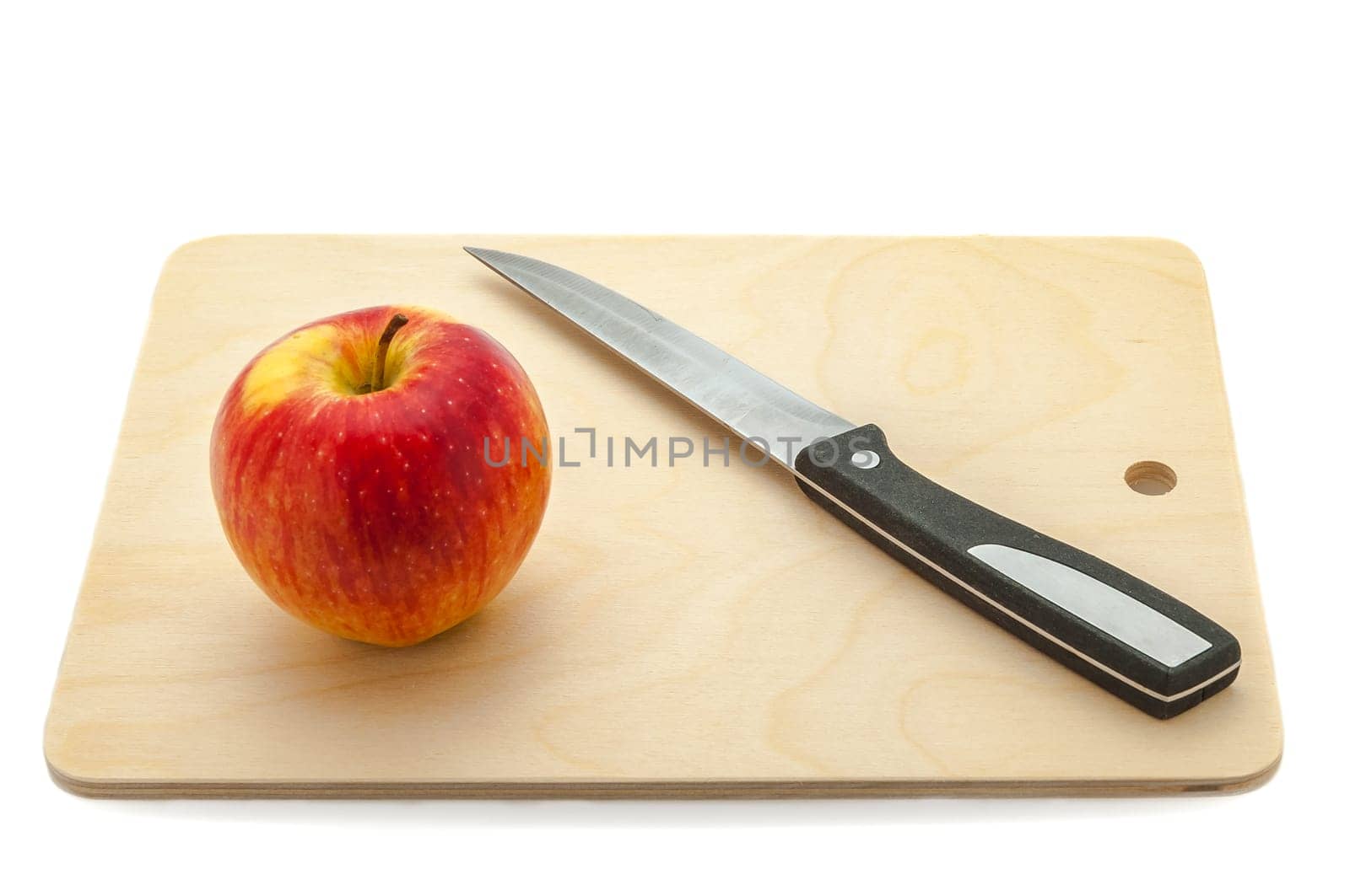 Red juicy apple and knife on a cutting board made of light wood.