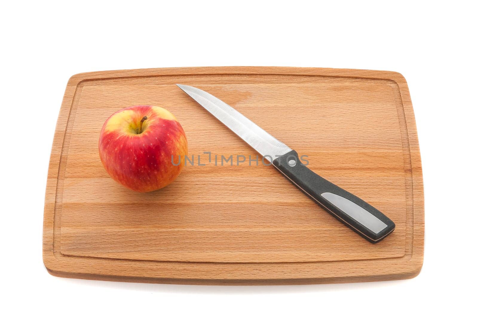 Ripe red juicy apple and knife on a cutting board made of dark wood.