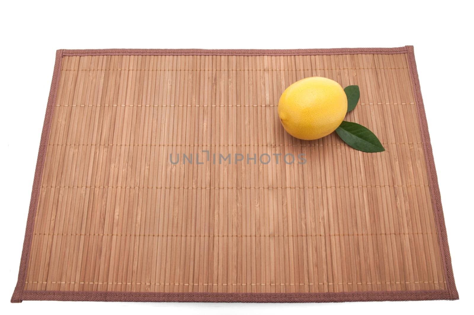 Lemon with leaves in the upper right corner on bamboo mat