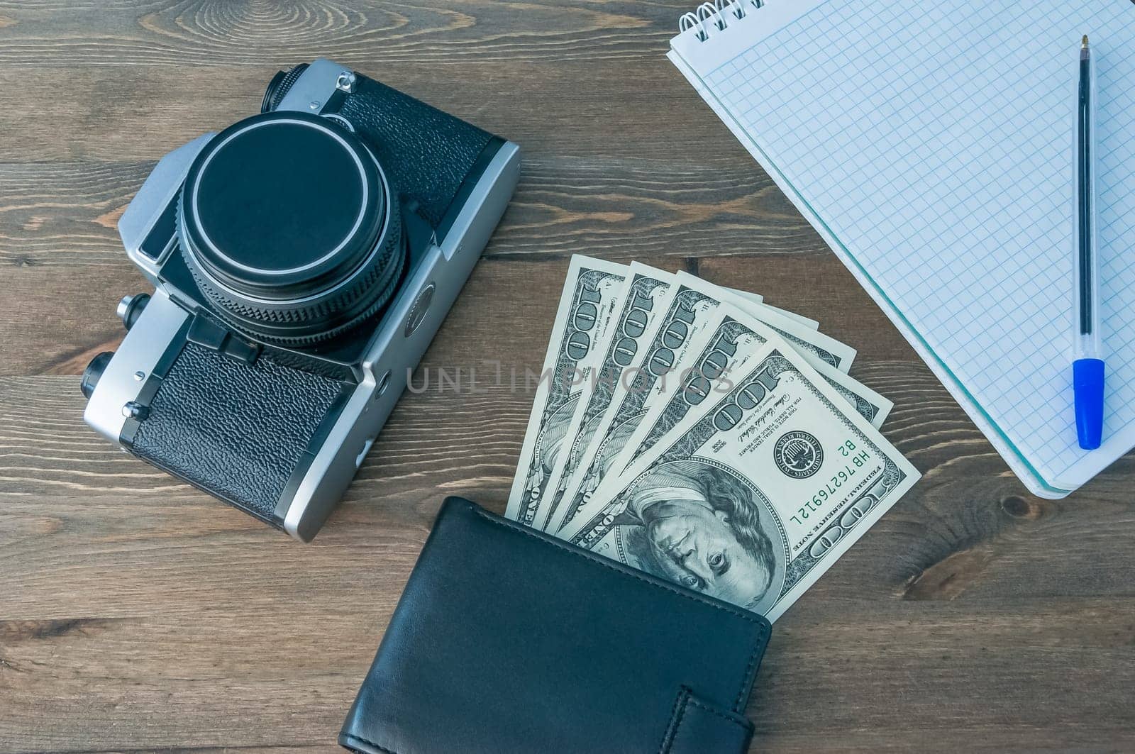 Retro camera, purse and notepad with pen on a wooden table.