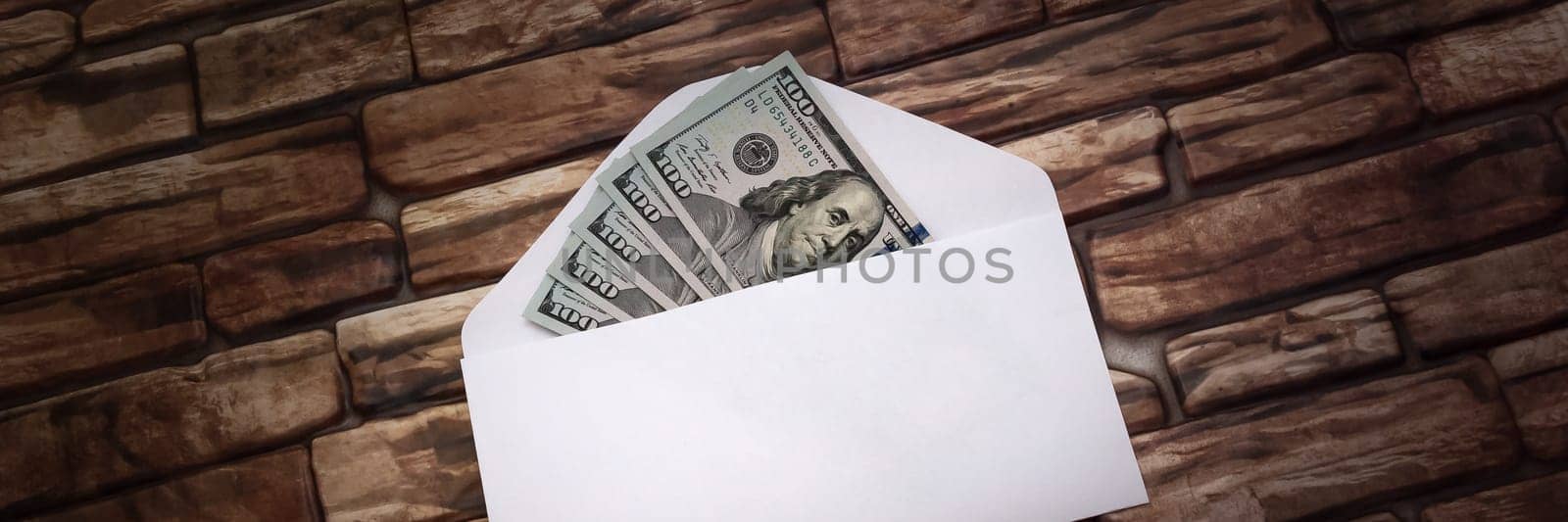 White envelope with five hundred dollar bills in a ray of light against a dark brick wall.