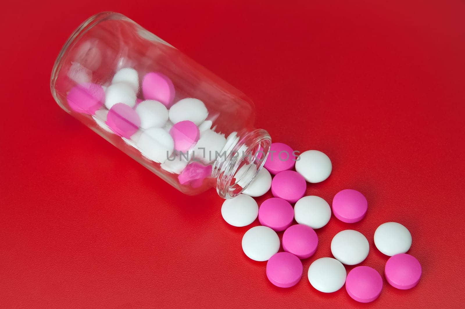 Pink and white pills scattered from a glass jar.