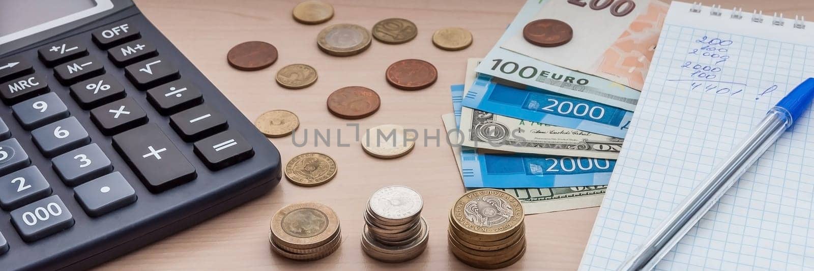 Notepad with a pen, bills, various money and a calculator on the table.