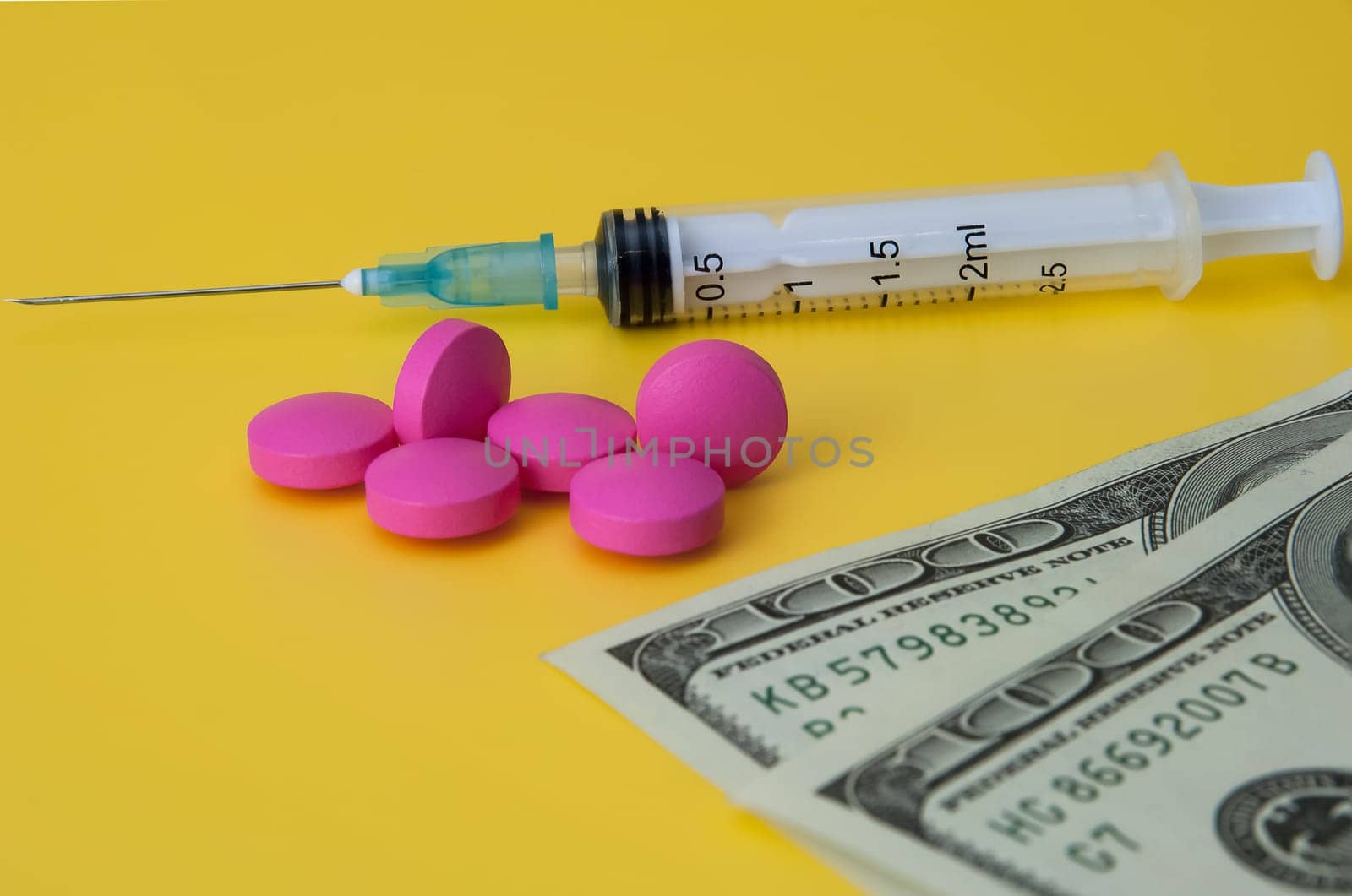 Syringe, pink large pills and dollars on a yellow background.