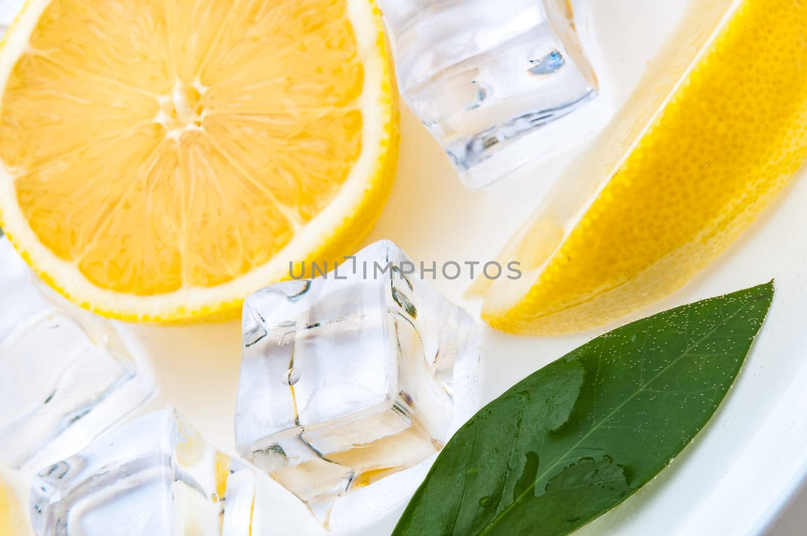 Half a bright lemon with a green leaf and cubes of refreshing ice close up